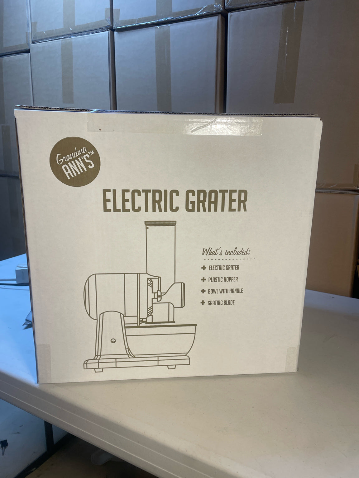 Grandma Ann's Electric Grater in its retail packaging, with stacked inventory cartons behind it
